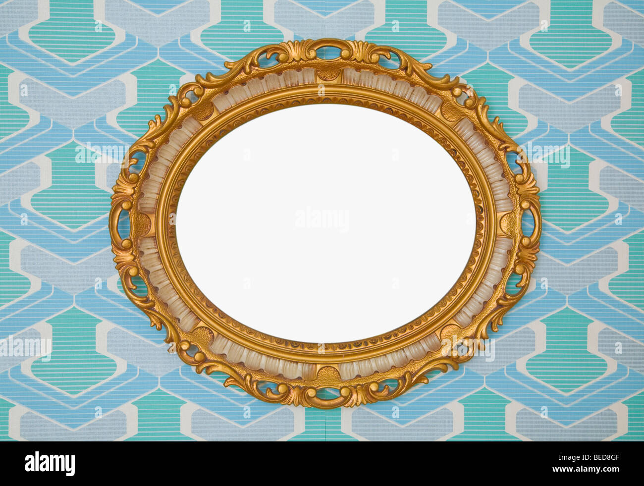 Kitschy golden plastic oval frame, horizontal, mounted on wallpaper from the 1960s or 1970s, frontal view Stock Photo