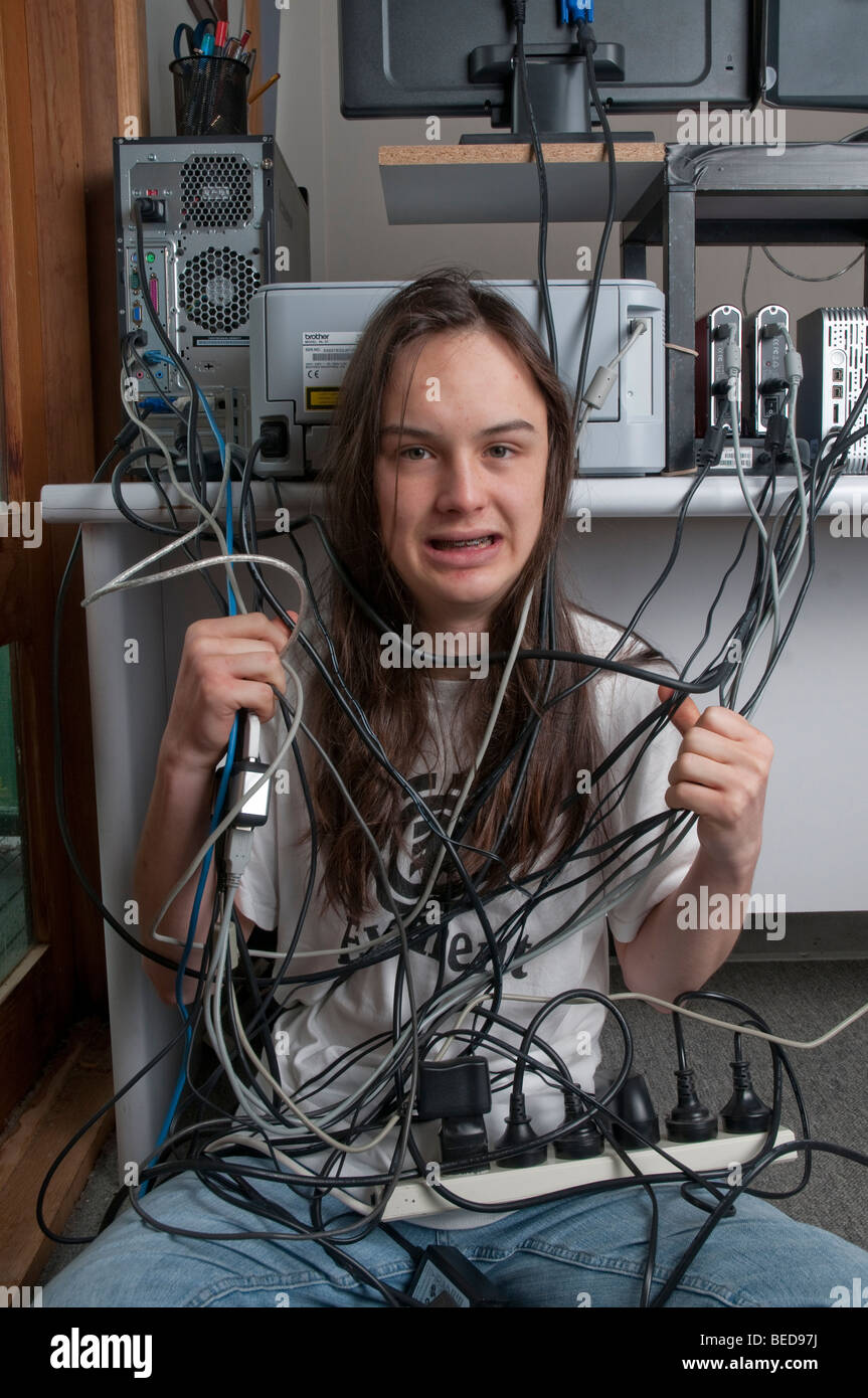 Long-haired teenage boy tangled in computer cables Stock Photo