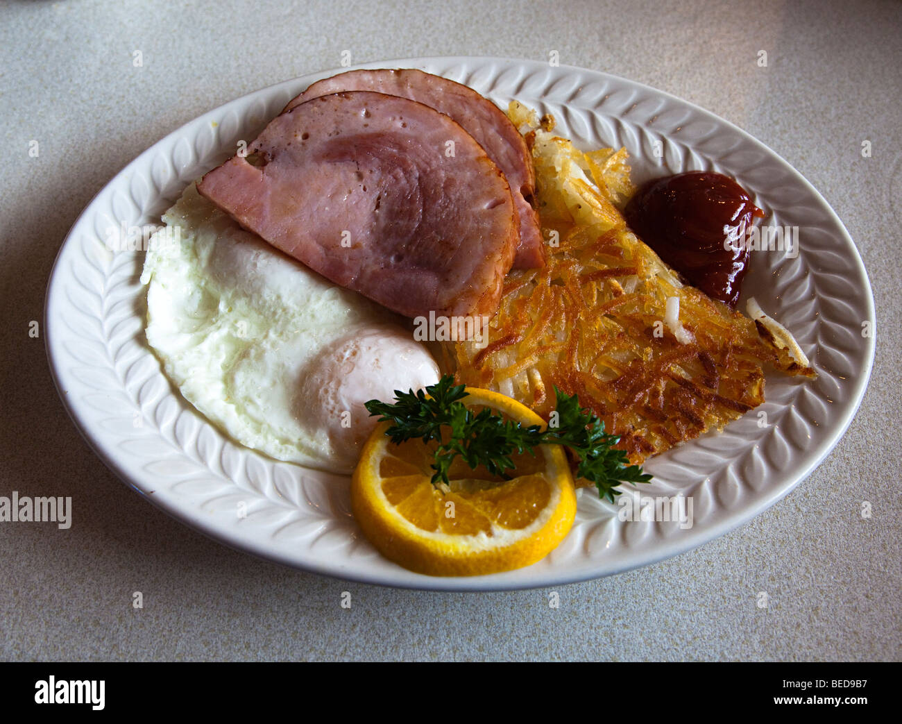 Breakfast in diner with fried egg hash browns ham orange and ketchup