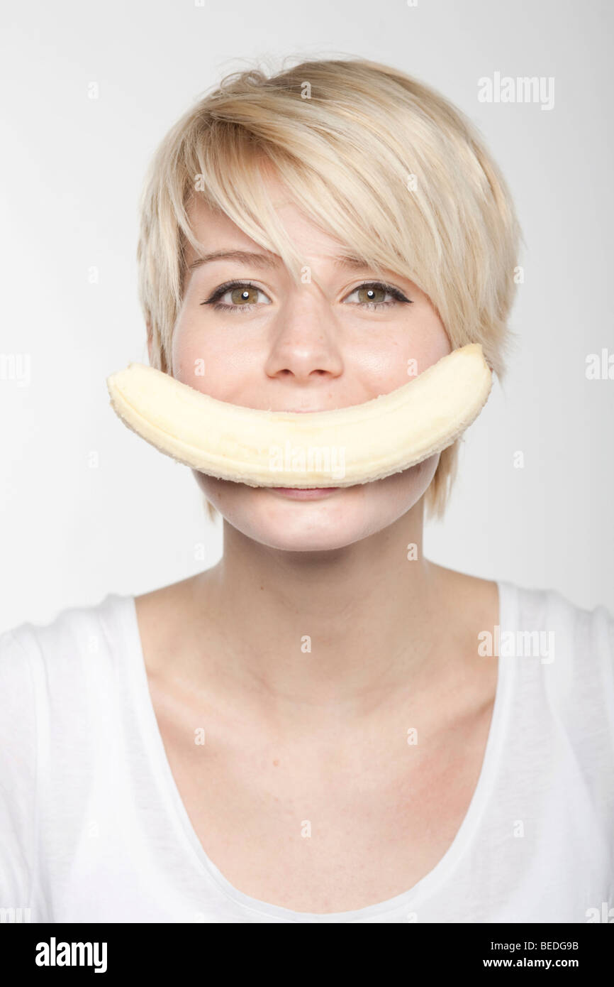Young woman with short blonde hair, banana in her mouth Stock Photo