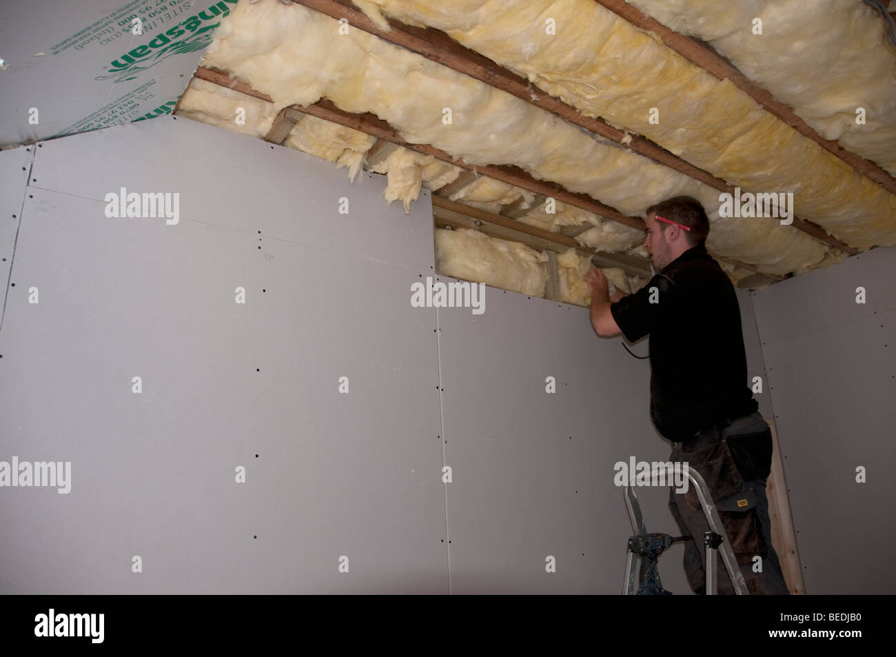 Fitting fibreglass insulation in stud wall and ceiling without safety goggles or mask Stock Photo