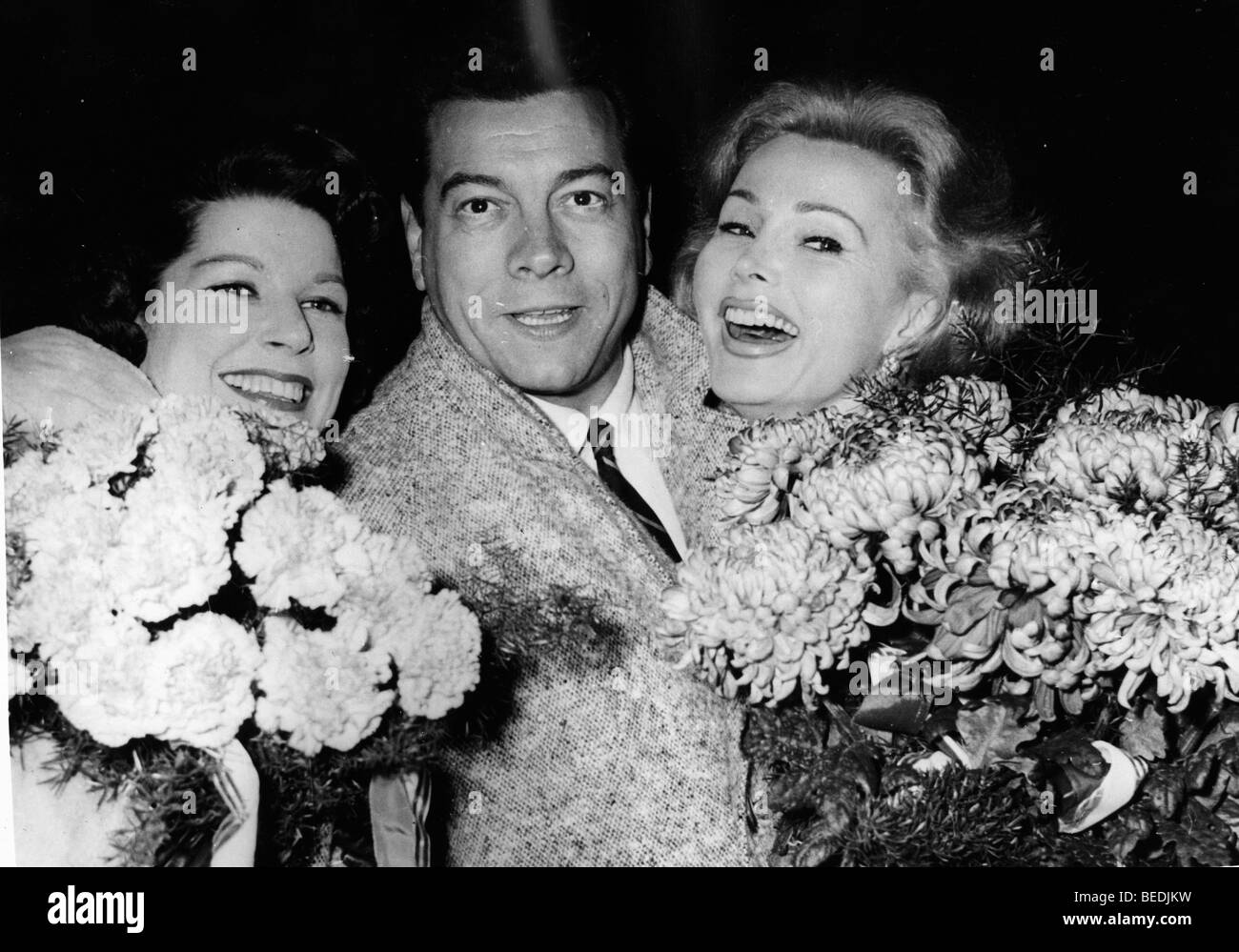 ZSA ZSA GABOR, right, laughs with two people and bunches of flowers. Stock Photo