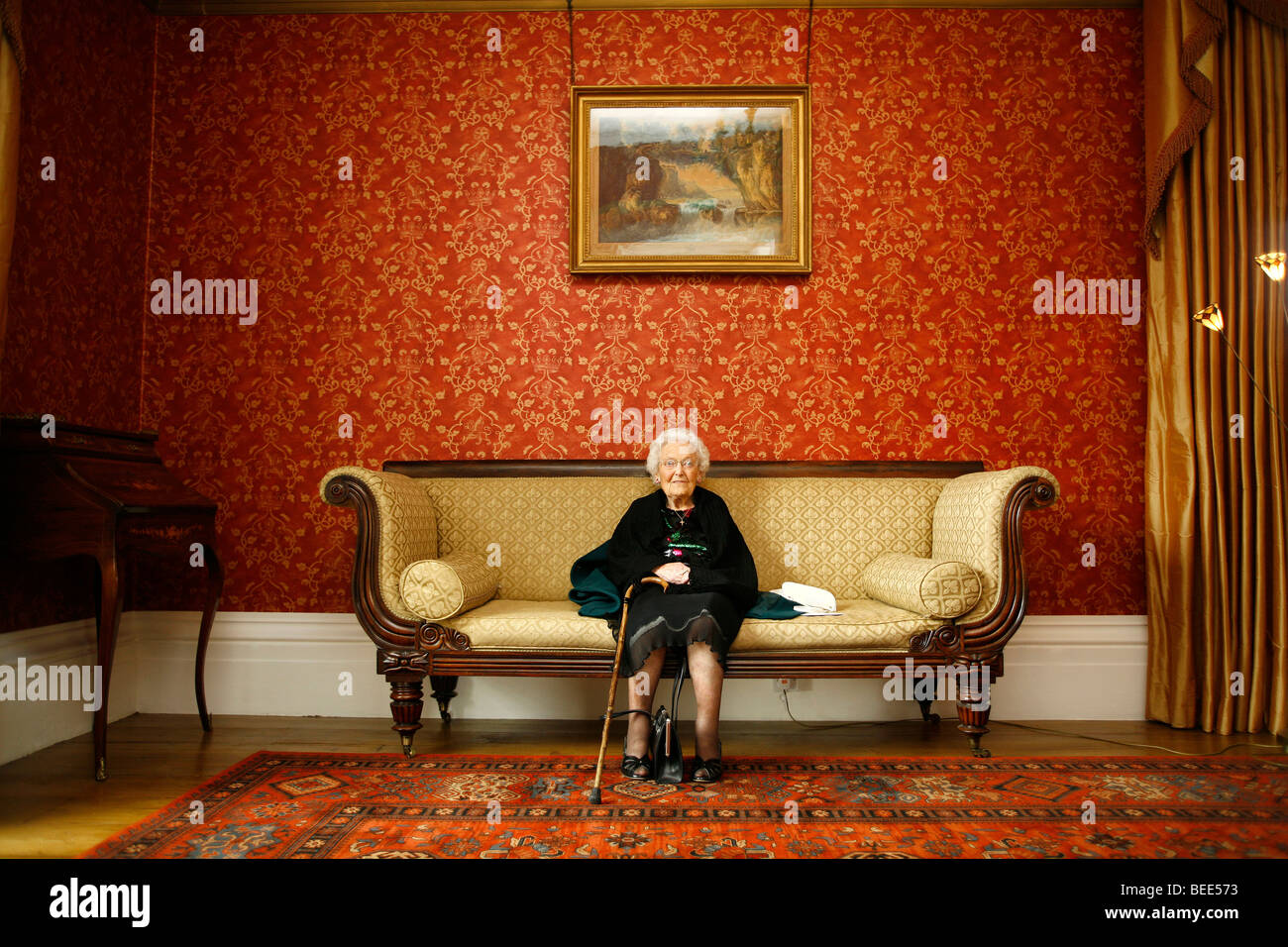 Smiling senior woman sitting alone on a sofa Stock Photo - Alamy