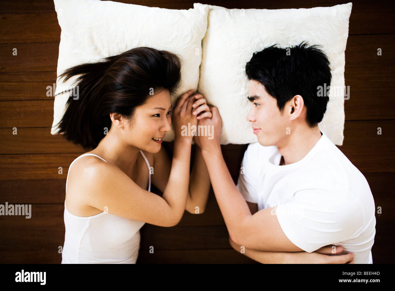 Asian Young couple lying on floor looking at each other smiling holding hands Stock Photo