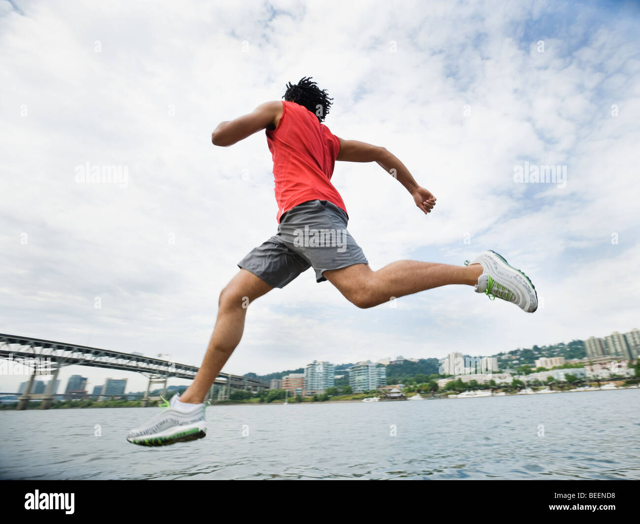 Mixed race man leaping next to river Stock Photo