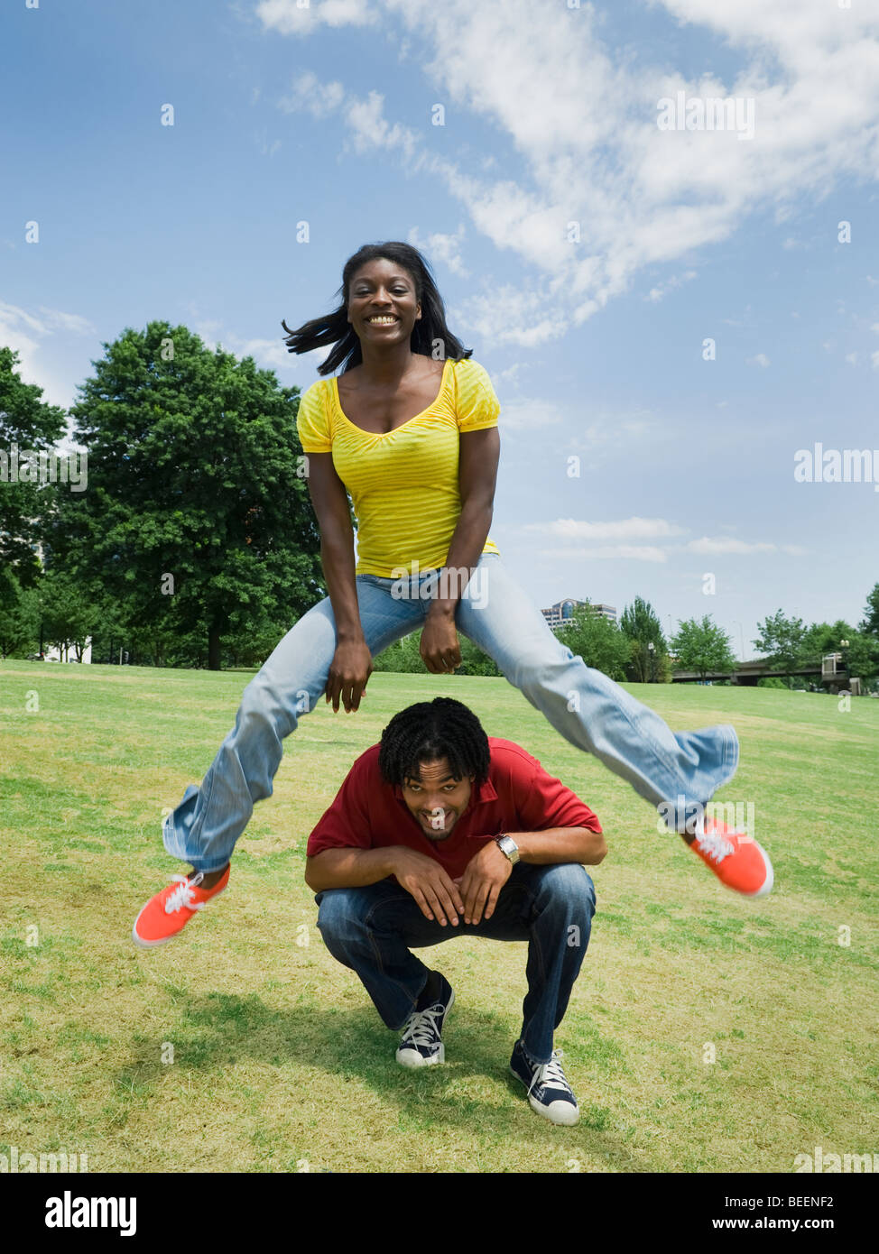 Woman leaping over man in park Stock Photo