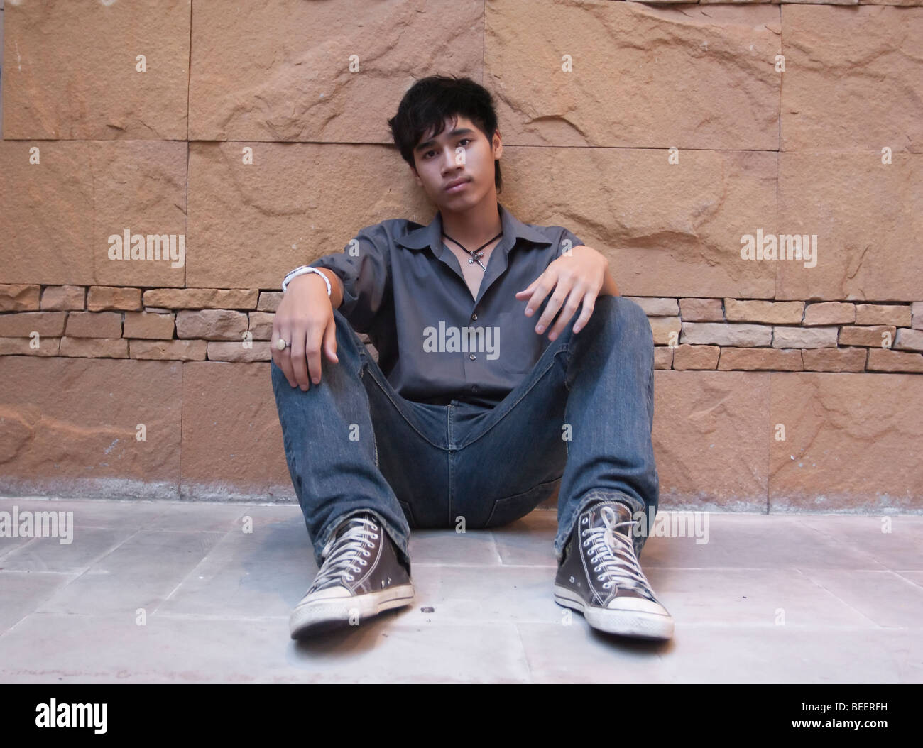 Asian man sitting against wall Stock Photo Alamy