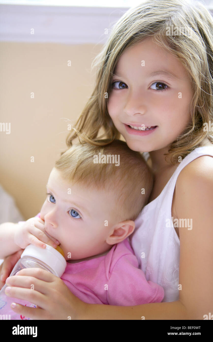 Toddler girl feeding bottle of milk to her baby sister Stock Photo Alamy