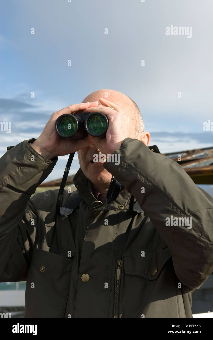 A man uses binoculars to look for sea birds on a ferry crossing in the Outer Hebrides, Scotland. Stock Photo