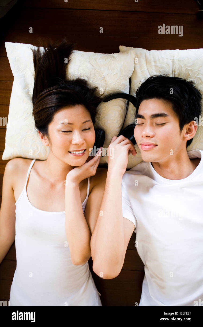 Asian Young couple lying on floor wearing headphones, eyes closed Stock Photo