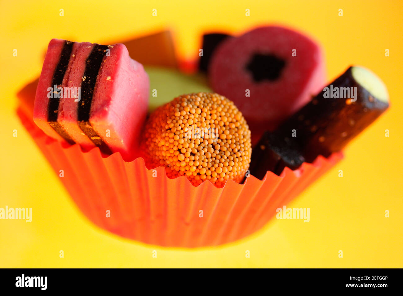 Liquorice Allsorts in orange cupcake paper case against yellow