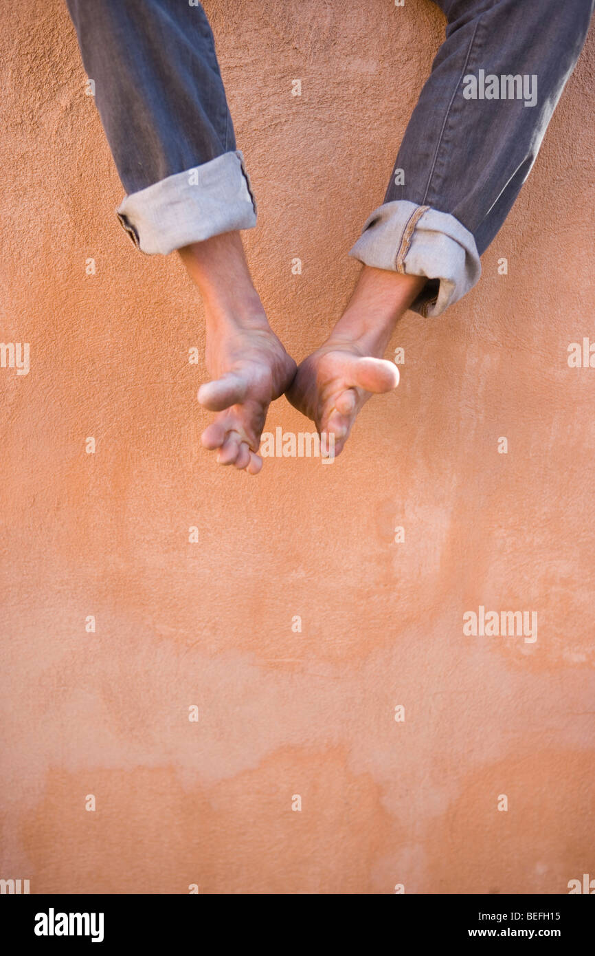 man dangling his feet against an adobe wall Stock Photo