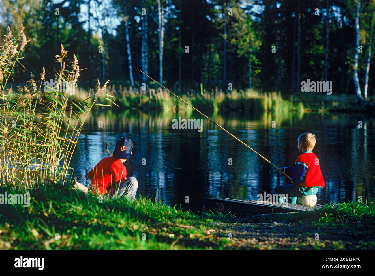 Two boys sitting on river bank fishing in sunset light in Sweden
