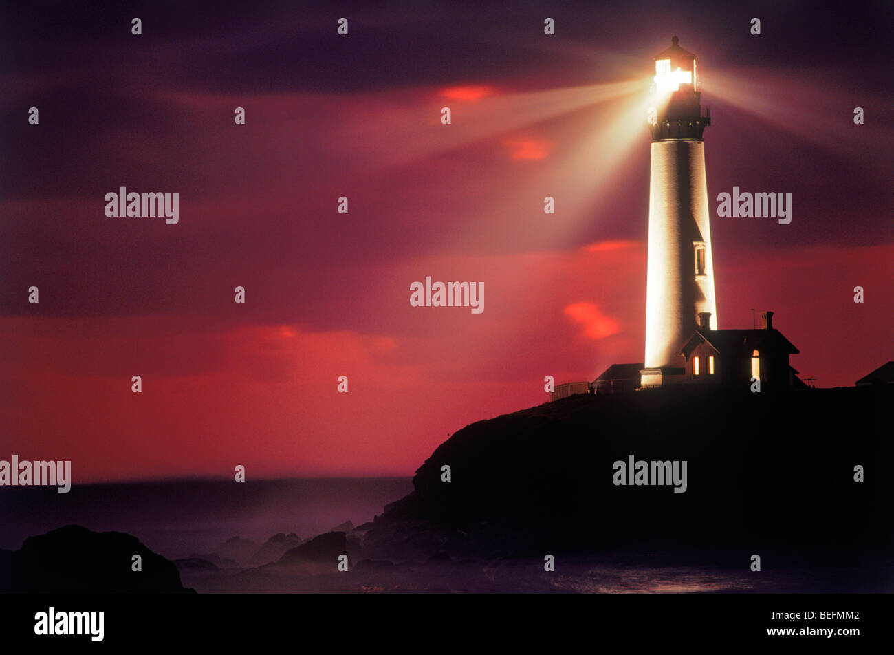 Pigeon Point Lighthouse casting beam across rocky shore and sunset skies. Image is not digitally altered - No photo shop.  REAL! Stock Photo