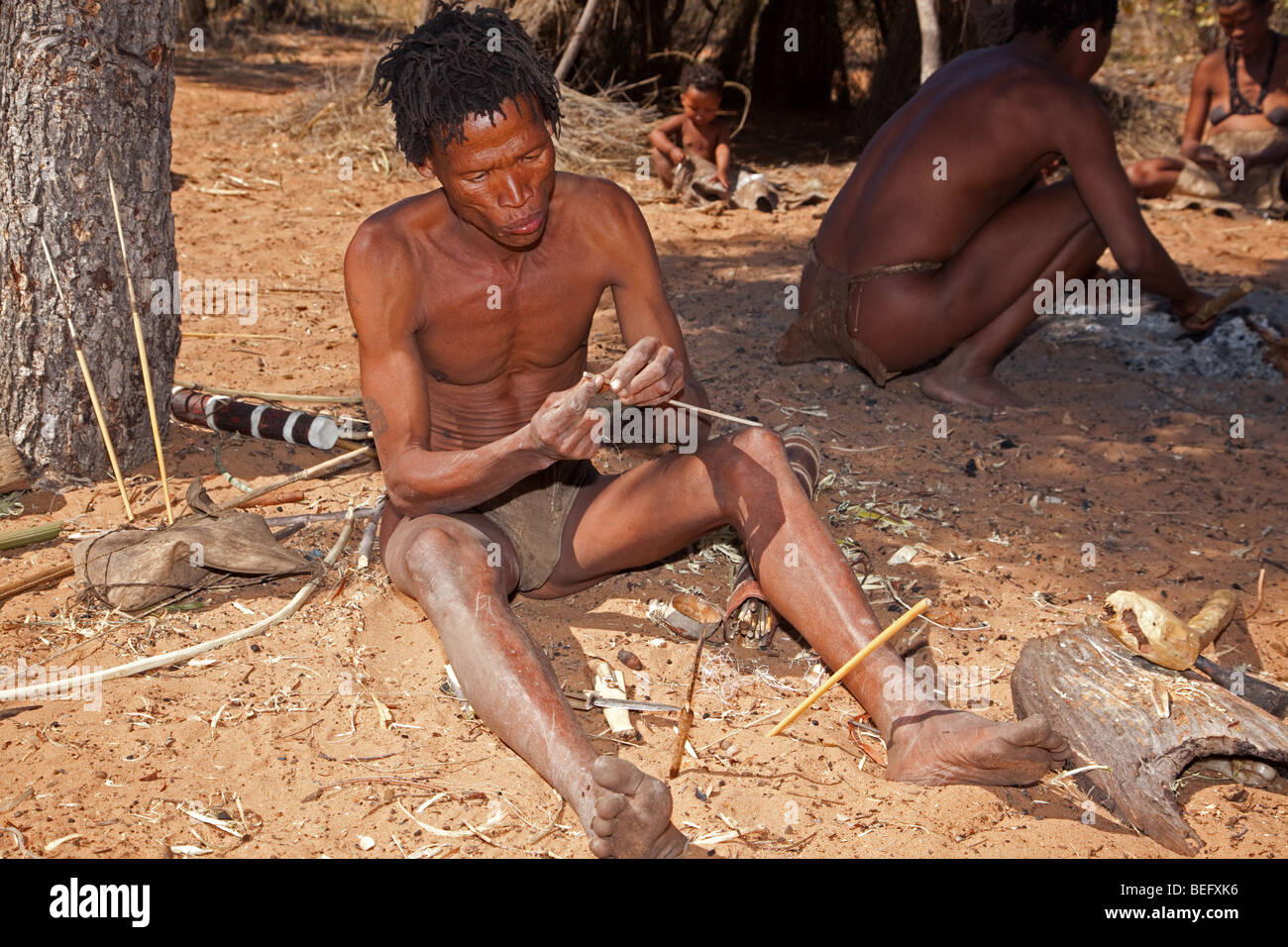 San Village. Manufacturing a bow and arrow the traditional way. Making the arrow. Stock Photo