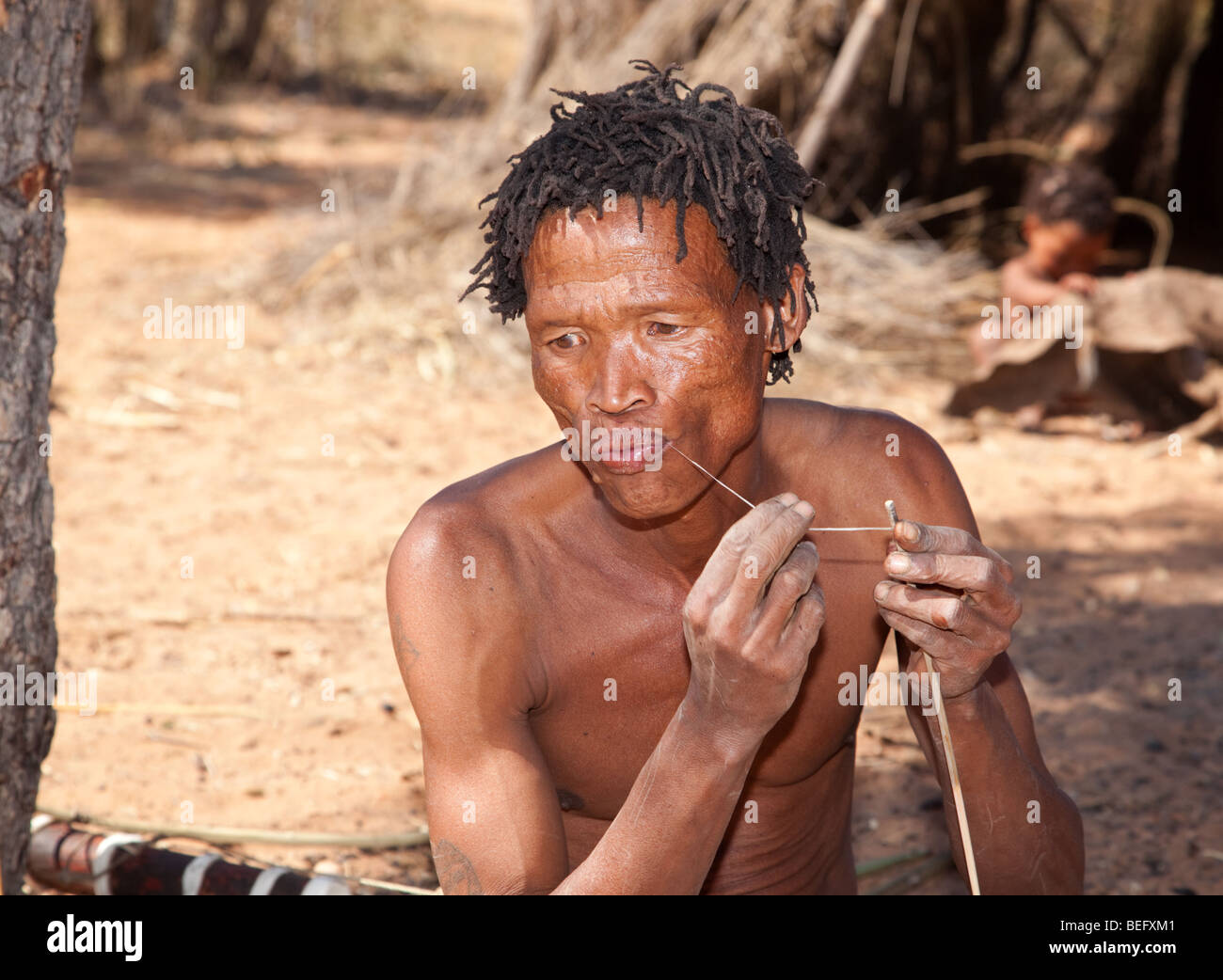 San Village. Manufacturing a bow and arrow the traditional way. Preparing the bow string. Stock Photo