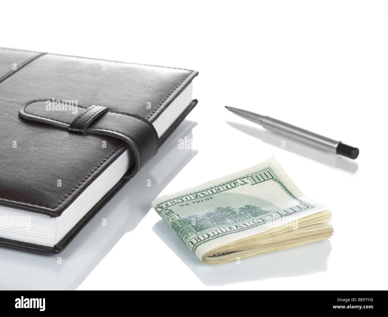 An agenda with several hundred dollar bills and a pen, isolated on white. Stock Photo