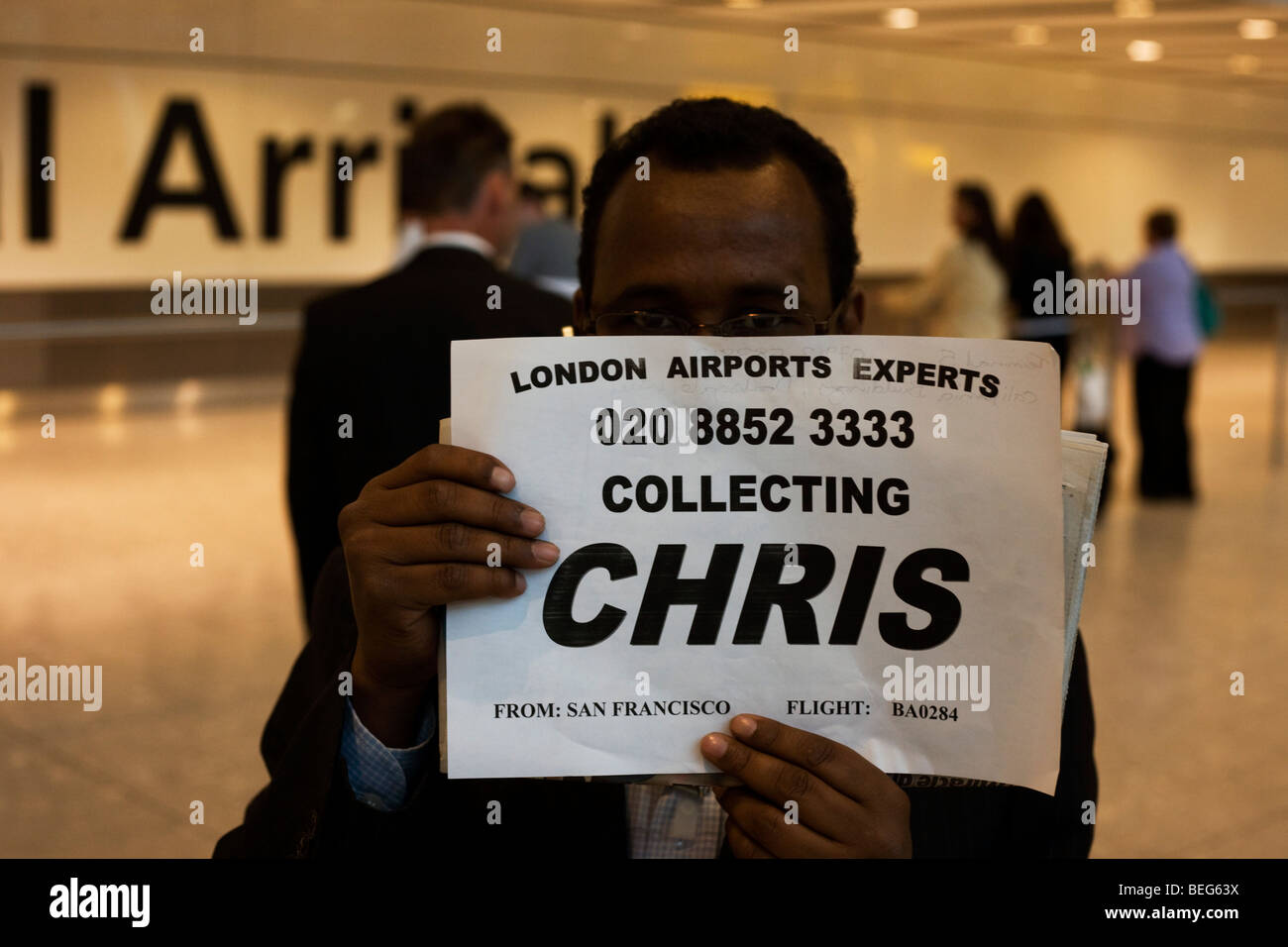 Greeting driver holding passenger name card in Arrivals at Heathrow's Terminal 5. Stock Photo