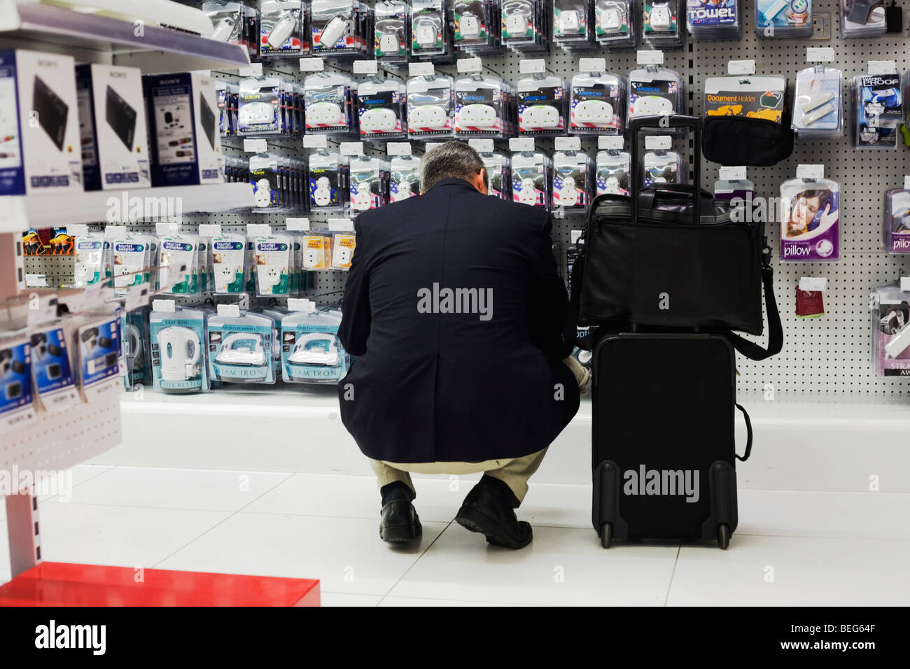 A passenger stoops to inspect travel adapters and plugs at Dixons Digital in Heathrow airport's terminal 5 Stock Photo