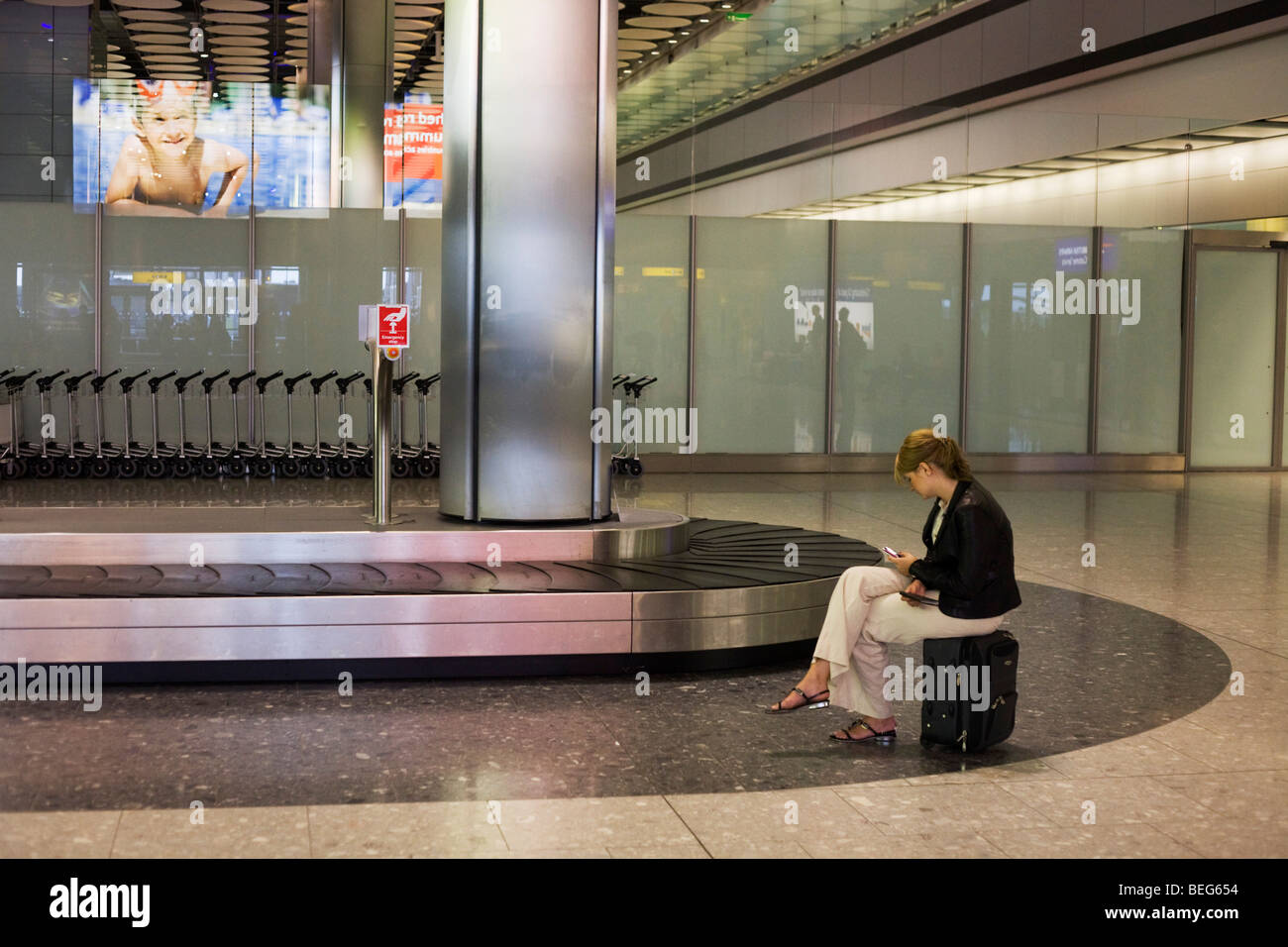 Lone lady awaiting her luggage from domestic baggage reclaim carousel at Heathrow's Terminal 5. Stock Photo