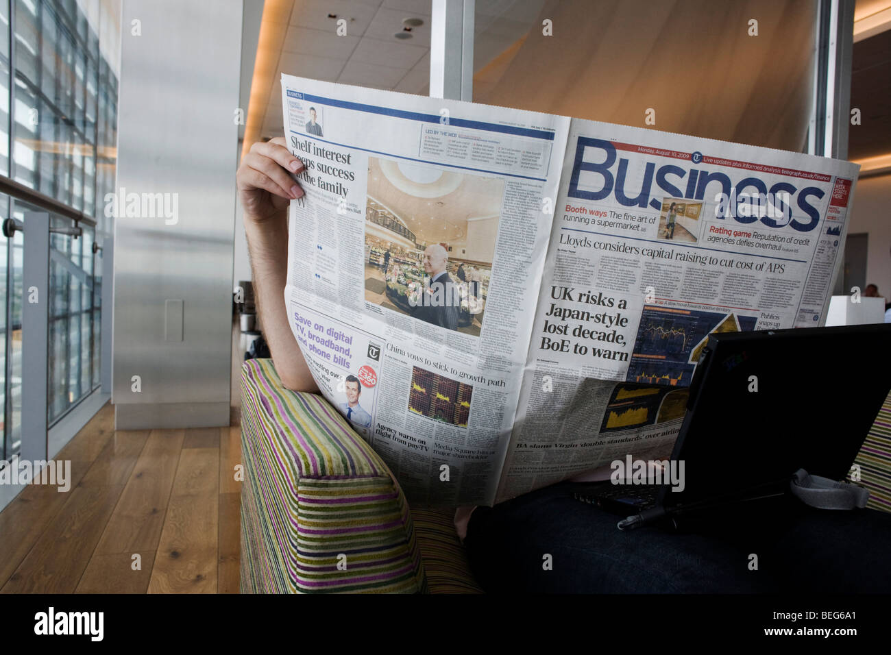 In the British Airways Galleries First lounge at Heathrow Airport's T5 a passenger reads the Business section of a broadsheet. Stock Photo