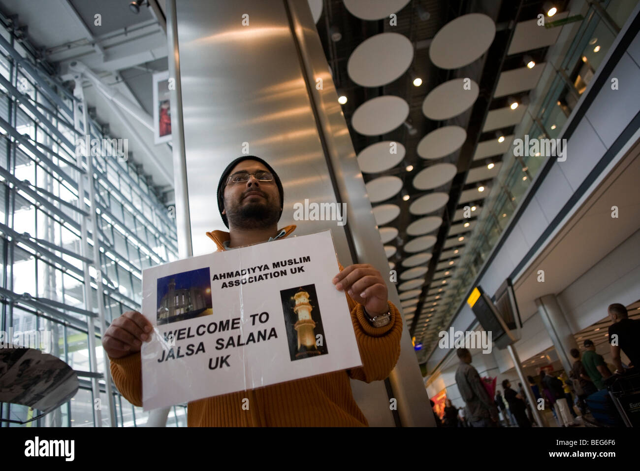 An Ahmadiyya mosque official holds a name card and awaits a fellow-Muslim in Arrivals at Heathrow airport's Terminal 5. Stock Photo