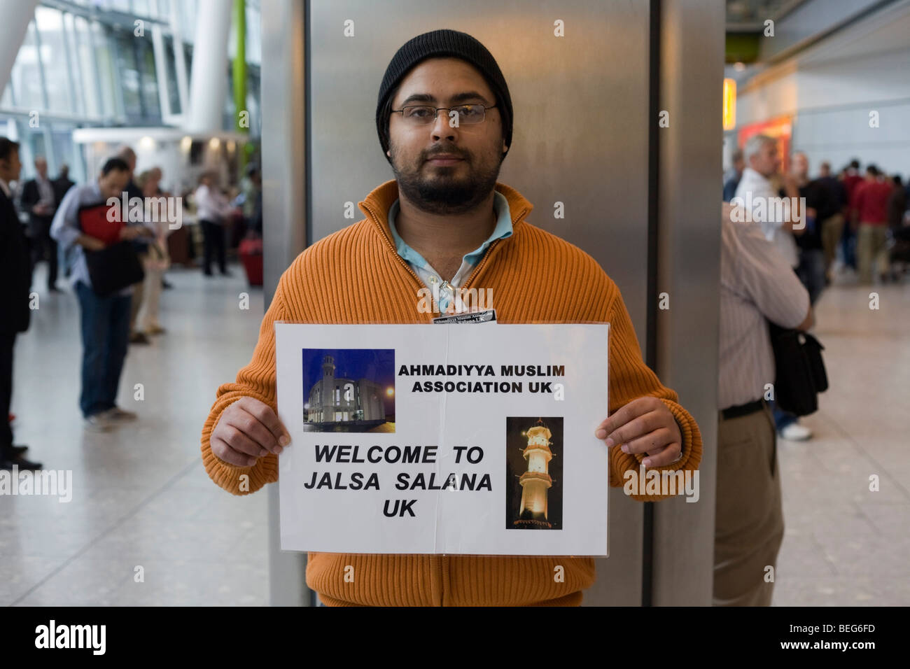 An Ahmadiyya mosque official holds a name card and awaits a fellow-Muslim in Arrivals at Heathrow airport's Terminal 5. Stock Photo
