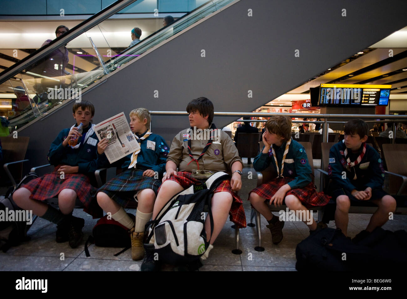 Wearing kilts, boys from a Scottish scout group sit and in the departures concourse of Heathrow Airport's Terminal 5. Stock Photo