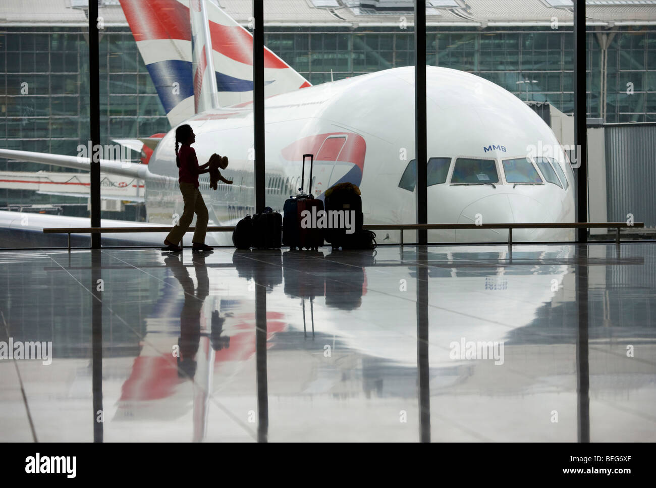 A young girl throws her pet toy tiger in front of a BA 777 airliner in a departure window of Heathrow Airport's T5 Stock Photo