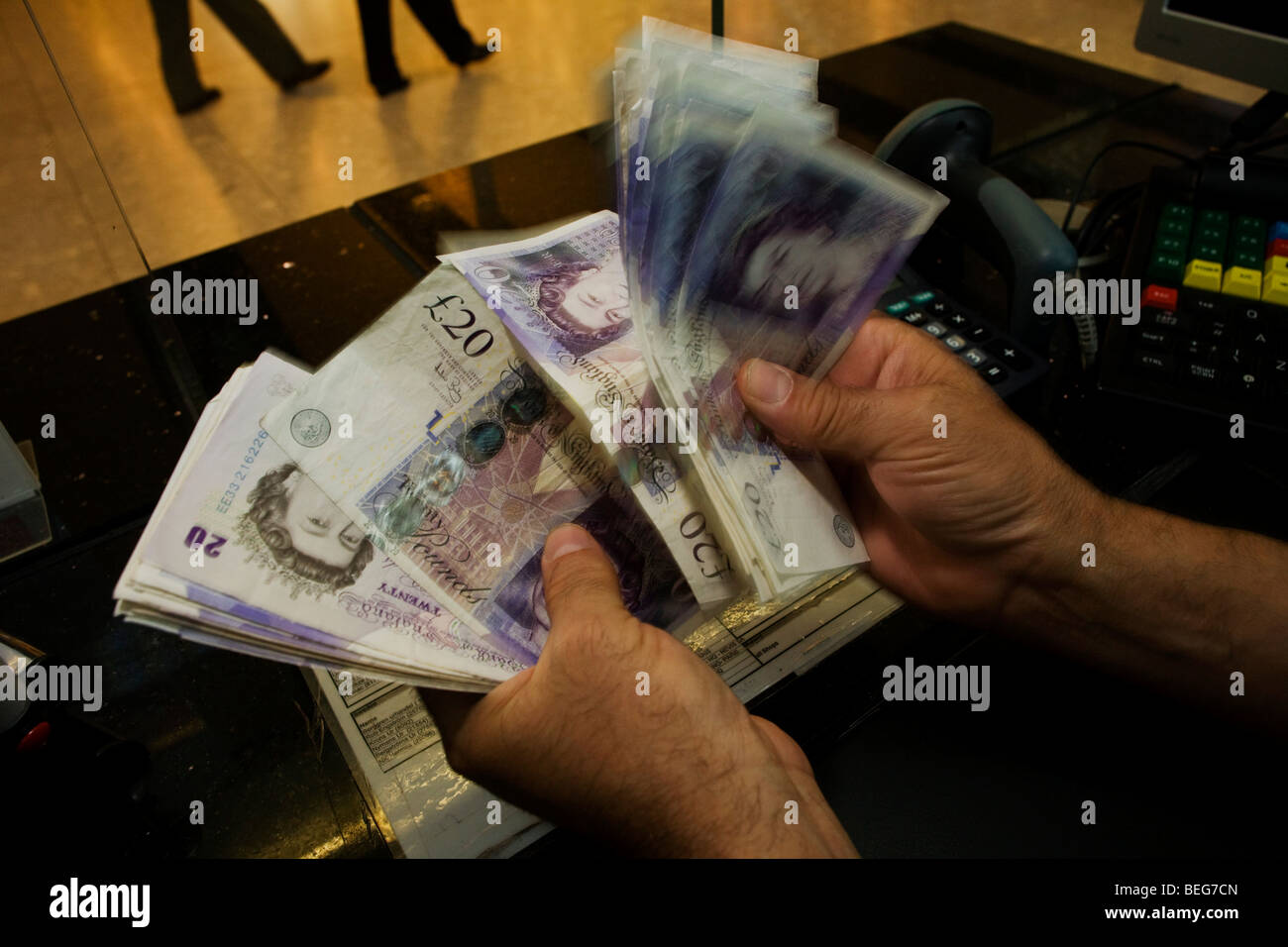 An assistant counts through blurred Pounds Sterling notes at the Travelex bureau de change at Heathrow Airport's Terminal 5. Stock Photo