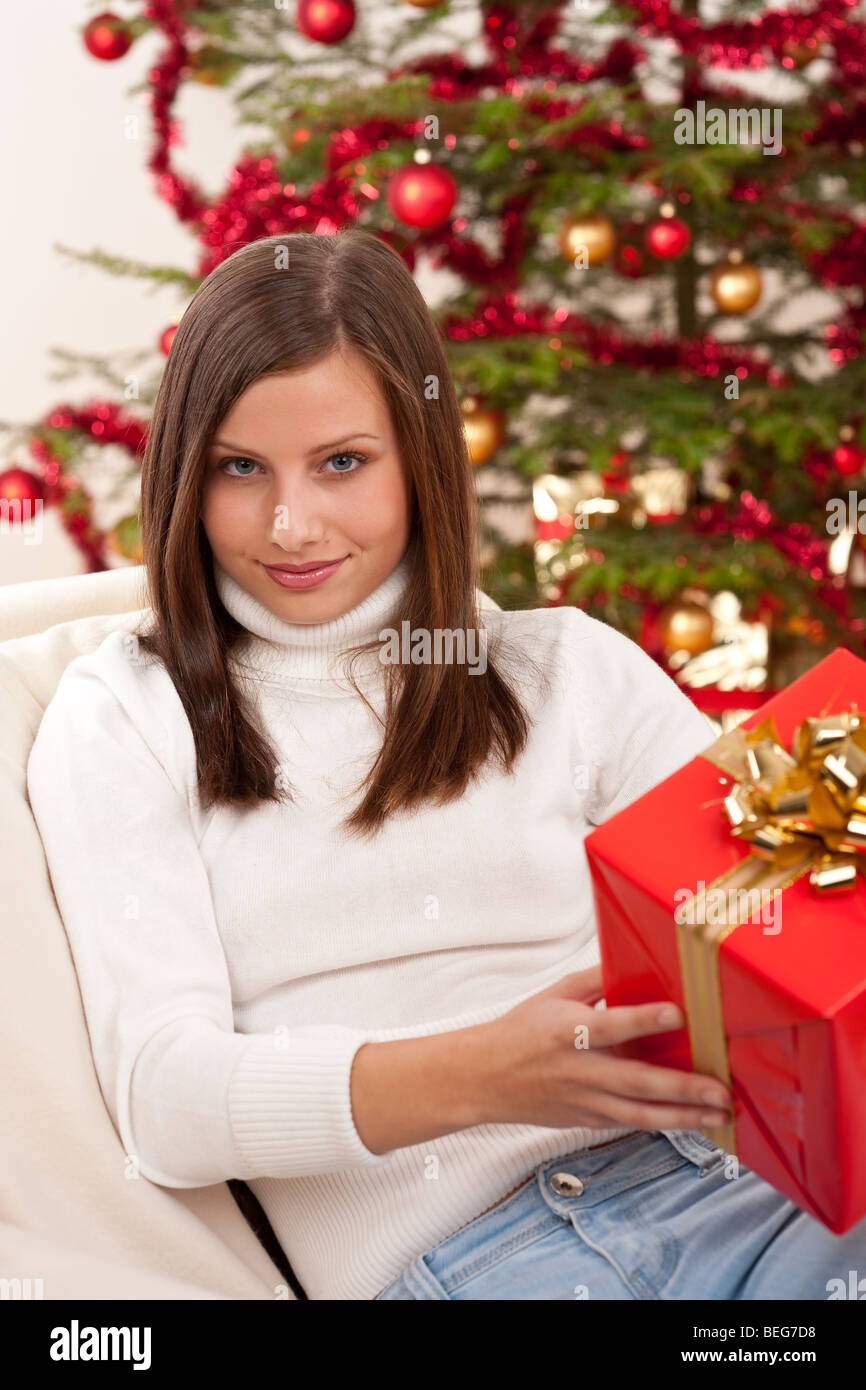Young woman holding Christmas present in front of tree Stock Photo - Alamy