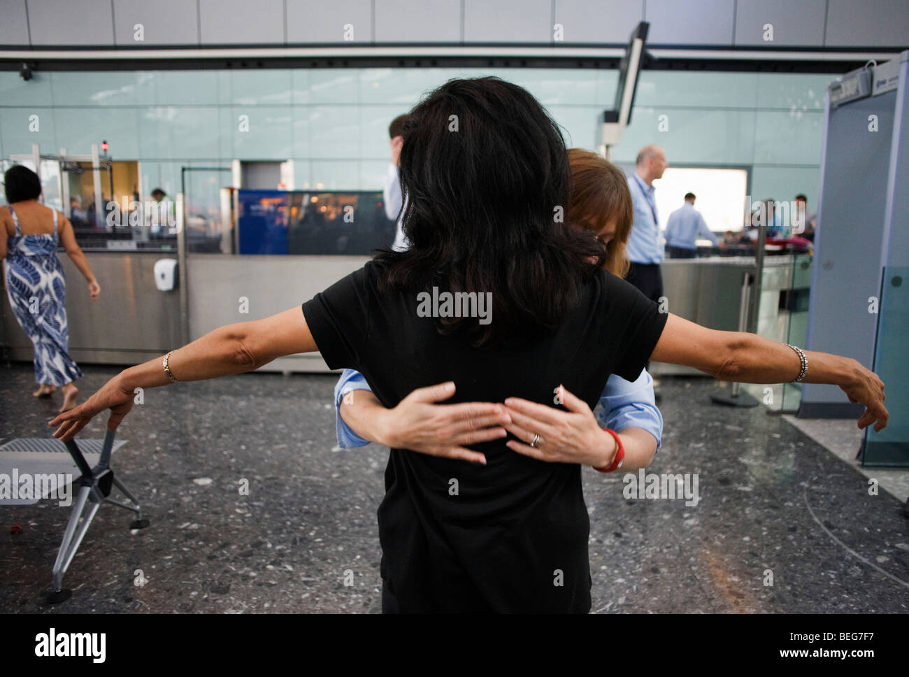 Female security operative feels around a lady passenger's back for suspect items during search at Heathrow Airport's T5 Stock Photo