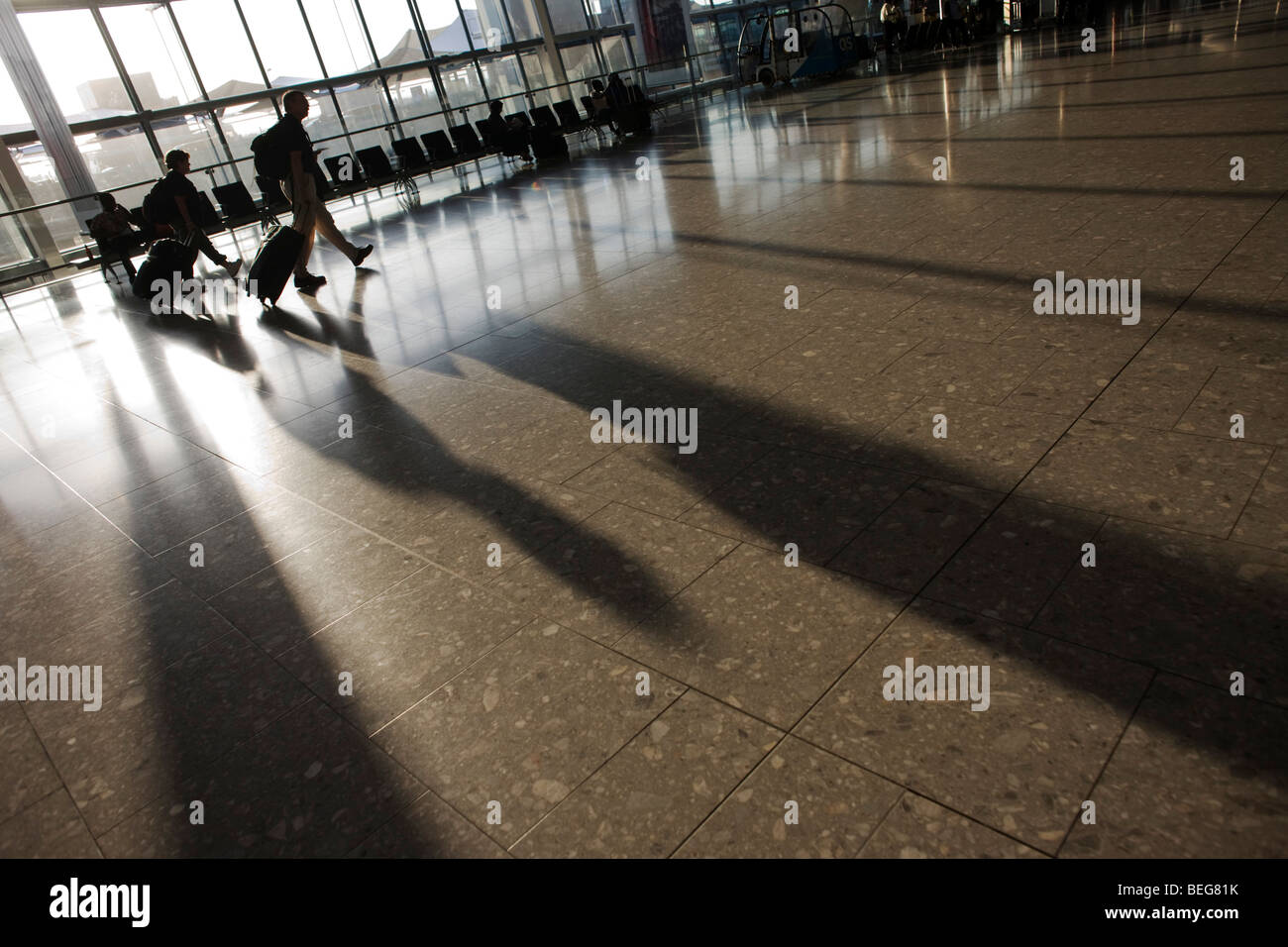Passengers walk through late sunlight that floods through large windows in departures concourse at Heathrow Airport's T5 Stock Photo