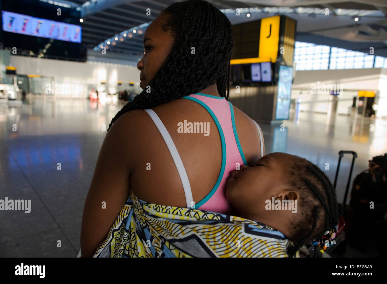 A young African mother allows her sleeping baby some well-earned rest on her back at Heathrow Airport's Terminal 5. Stock Photo