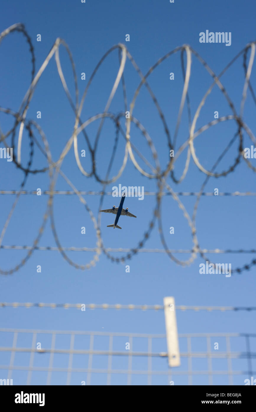An airliner crosses the razor-wired perimeter fence at Heathrow Airport on its way to an international destination. Stock Photo