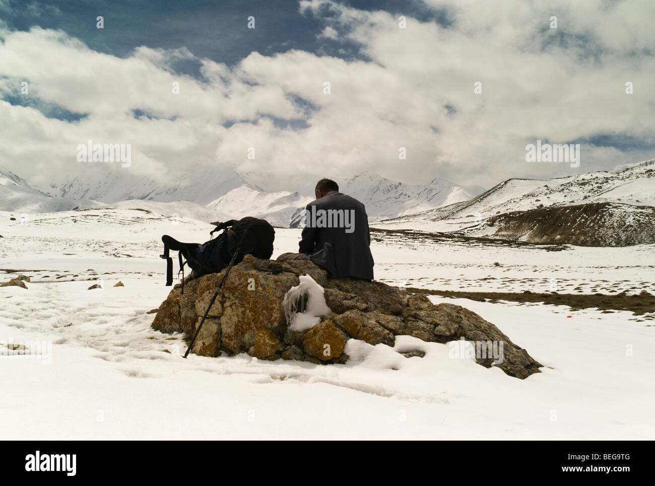 Man with backpack resting on a rock surrounded by snow in the Caucasian Mountains Stock Photo