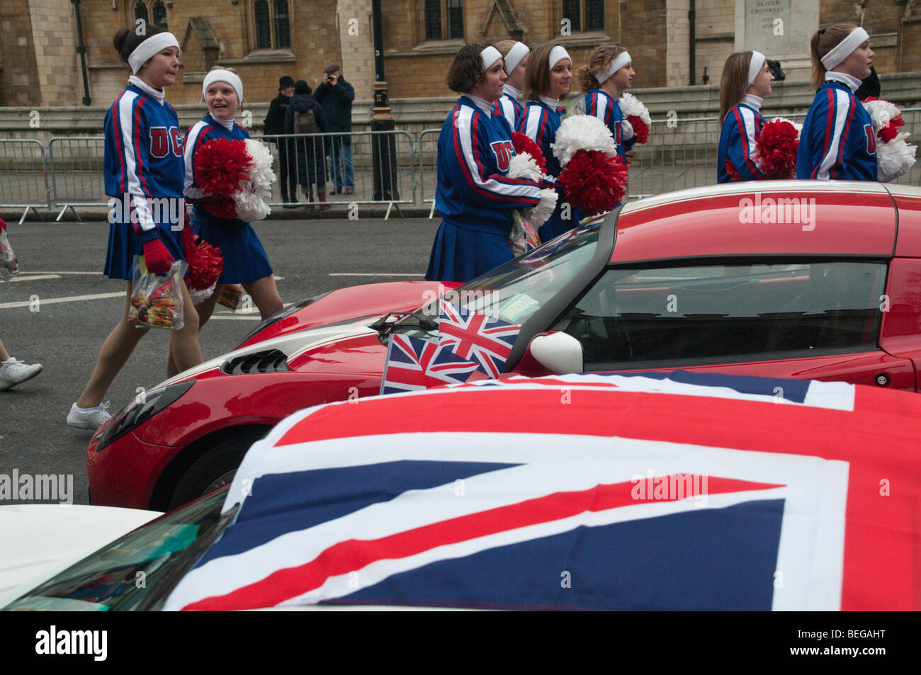 US cheer leaders with pompoms walks past cars with Union Jacks, London
