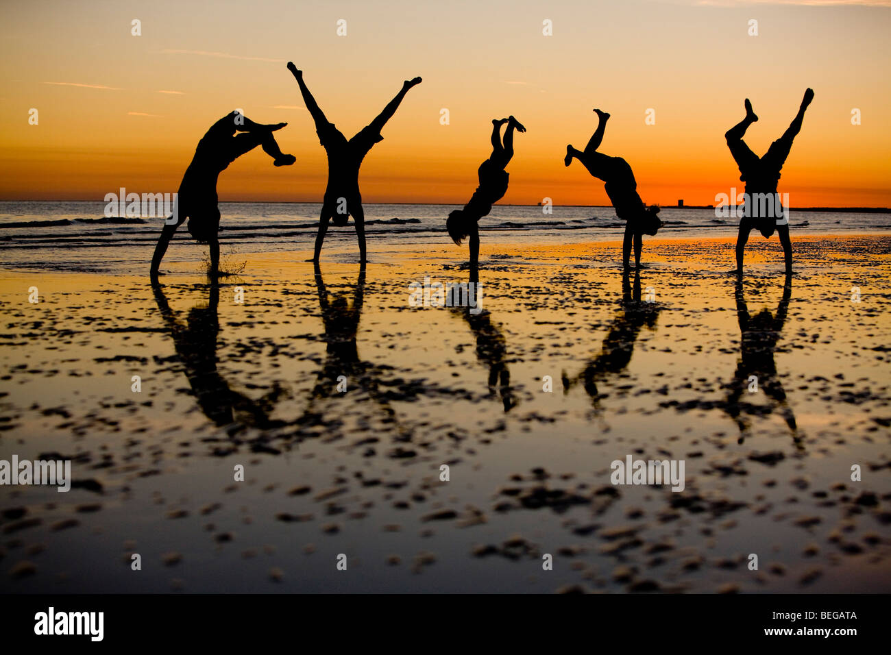 Friends playing on the beach silhouetted against an evening sky. Stock Photo