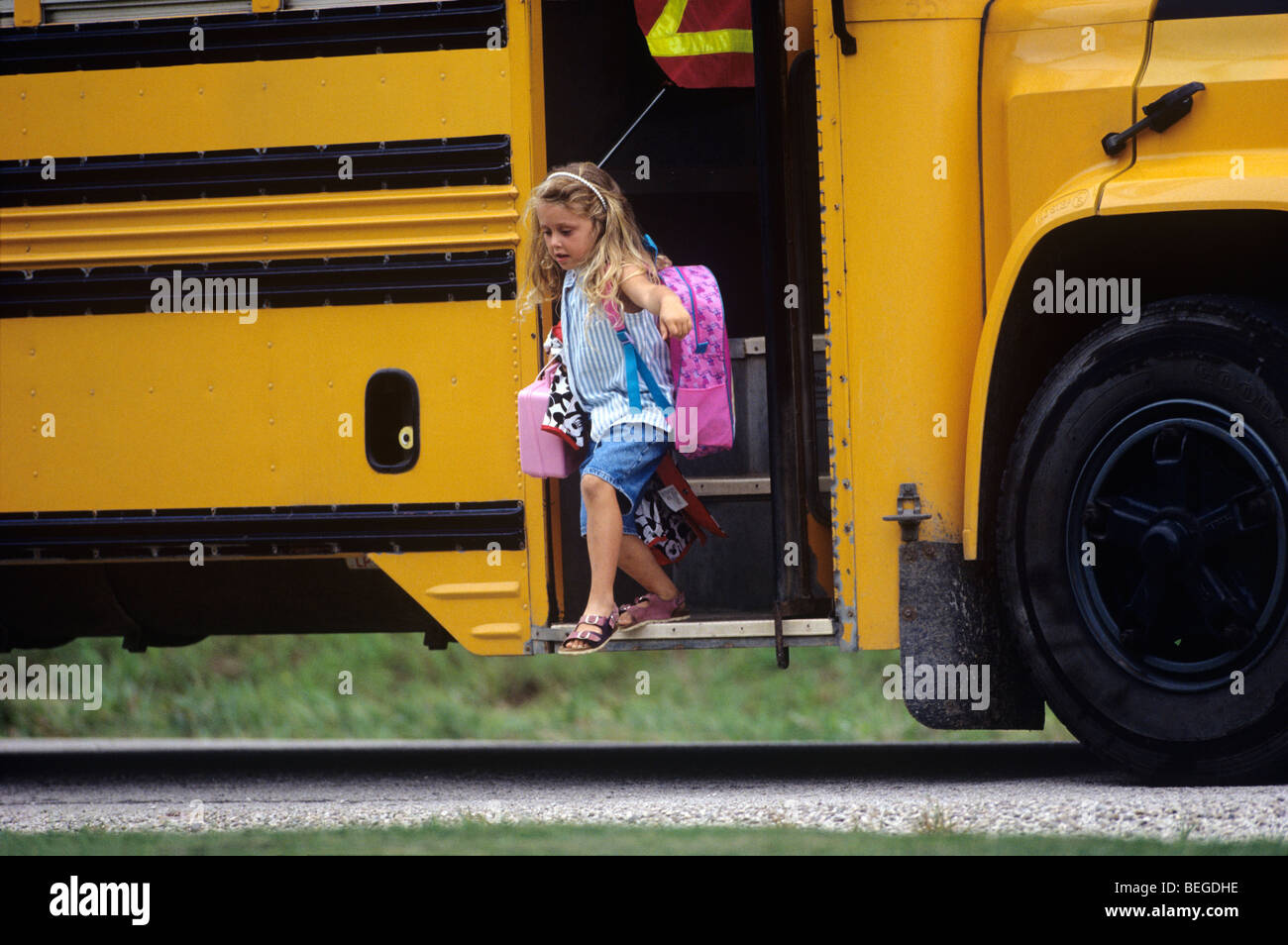 grade school girl student stepping off school bus with backpack and