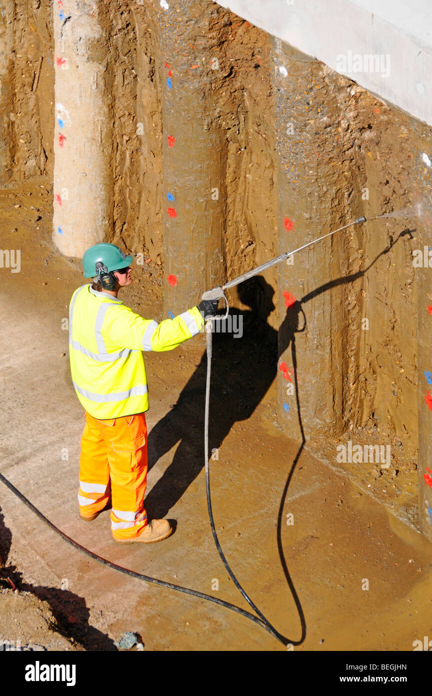 Retaining wall on building construction site worker high pressure water jet clean clay off new concrete piles M25 motorway widening Essex England UK Stock Photo