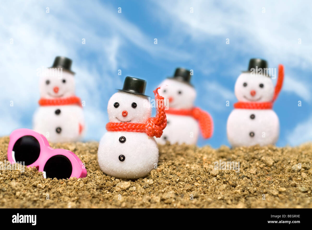 Christmas snowmen ornaments on a gravel beach with pink sunglasses to cast a tropical summer theme. Stock Photo
