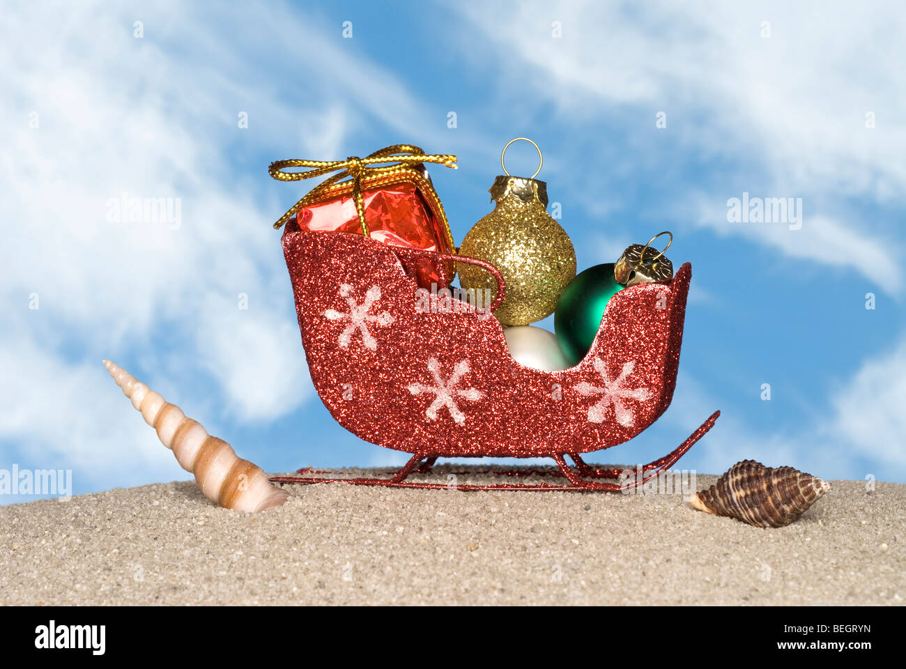 Santa's sleigh, loaded with ornaments and presents, on a sandy beach with seashells. Stock Photo