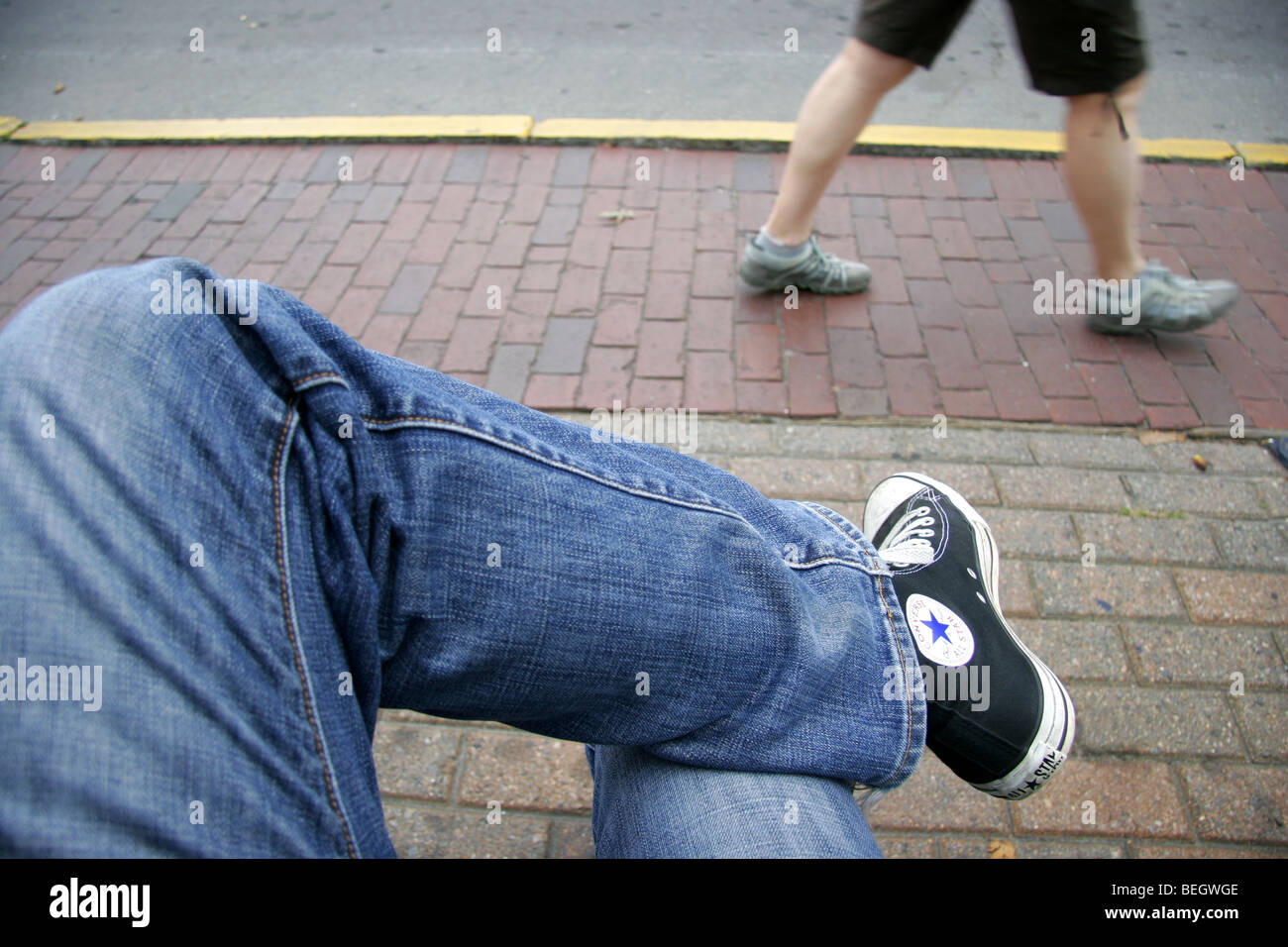 Person in jeans and Converse shoes sitting crossed legged outside as a  second person walks past Stock Photo - Alamy