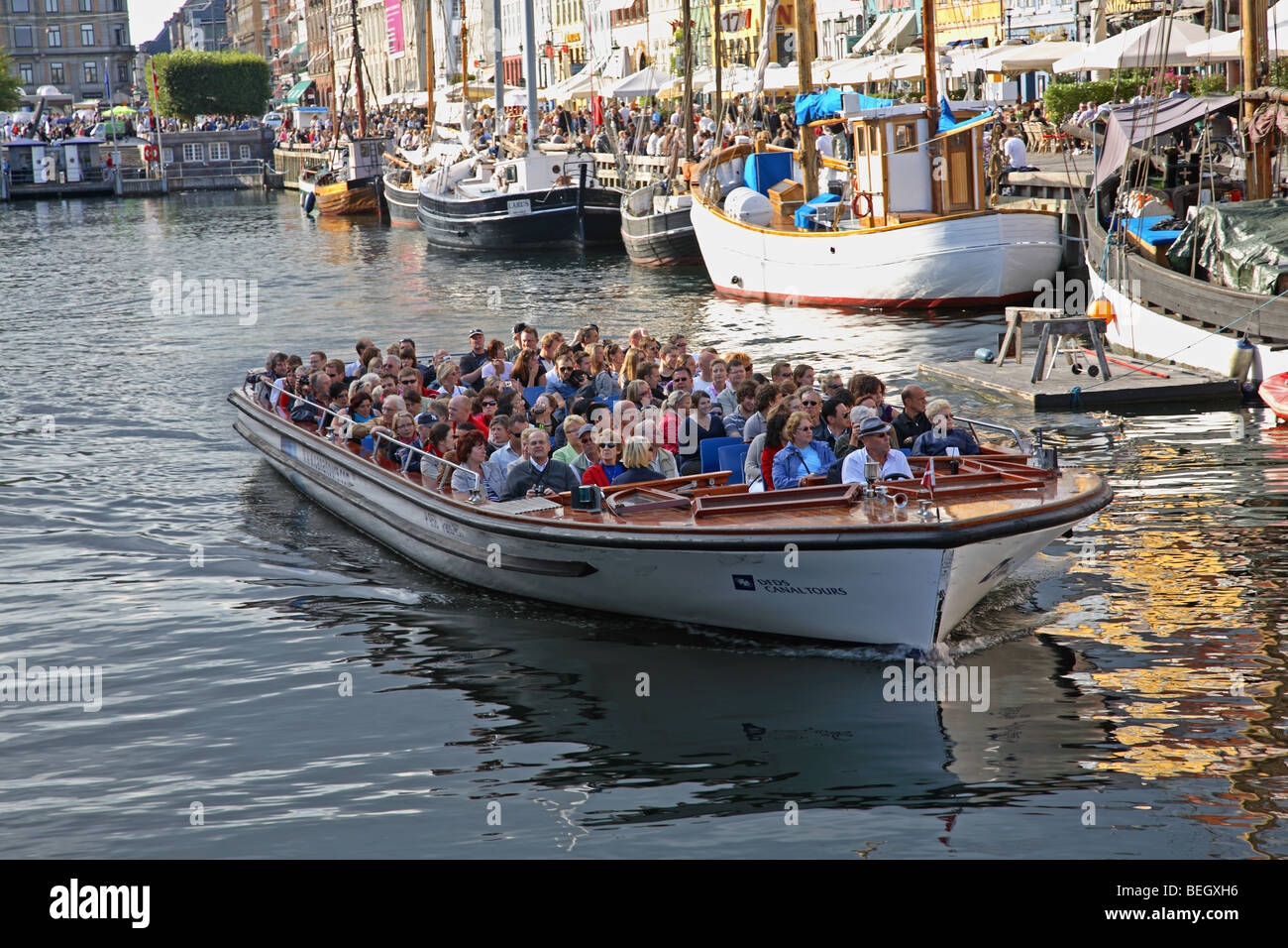 A canal tour cruise boat leaving Nyhavn in Copenhagen on a sightseeing tour just below the many waterside restaurants Stock Photo
