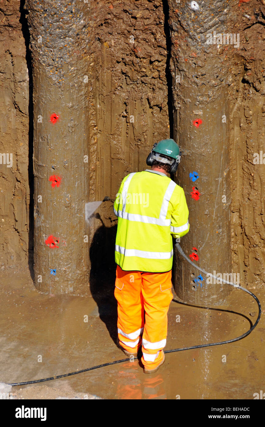 Retaining wall on building construction site worker high pressure water jet clean clay off new concrete piles M25 motorway widening Essex England UK Stock Photo