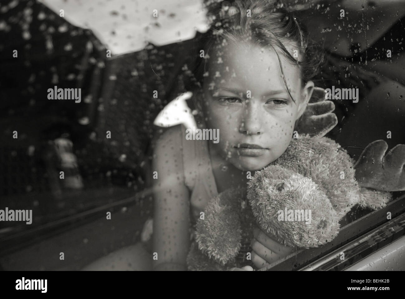 Sad little blonde girl portrait in the rain trough the glass window Stock Photo
