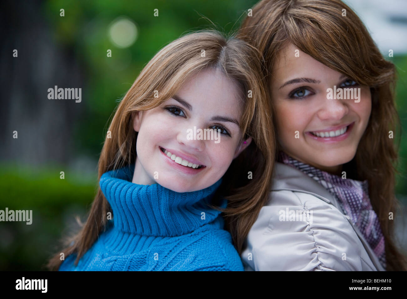 Portrait of two young women back to back and smiling Stock Photo - Alamy