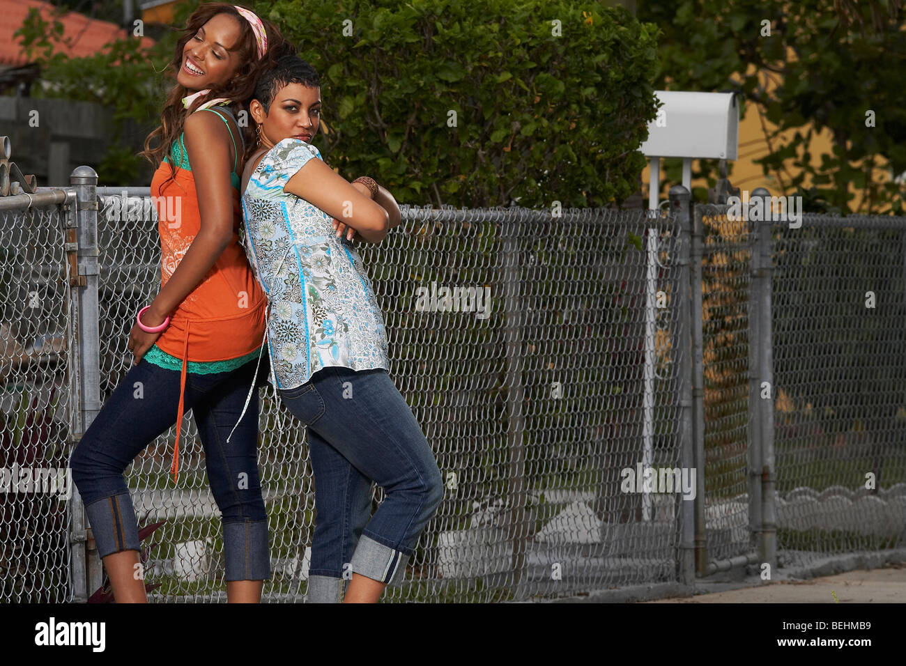 Two young women standing back to back and smiling Stock Photo - Alamy