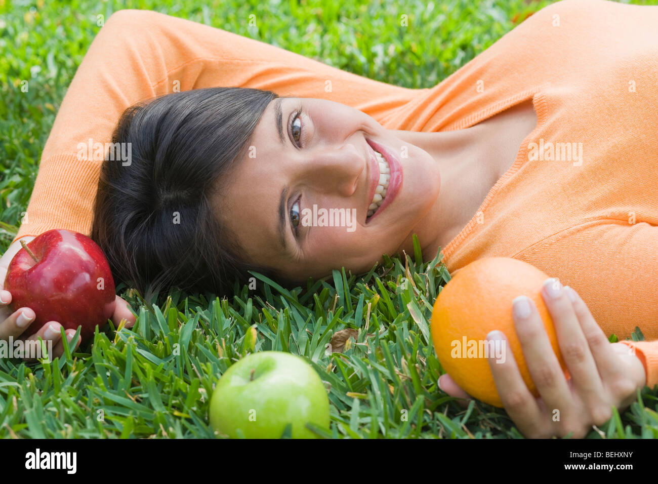 Teenage girl lying on grass and holding fruits Stock Photo