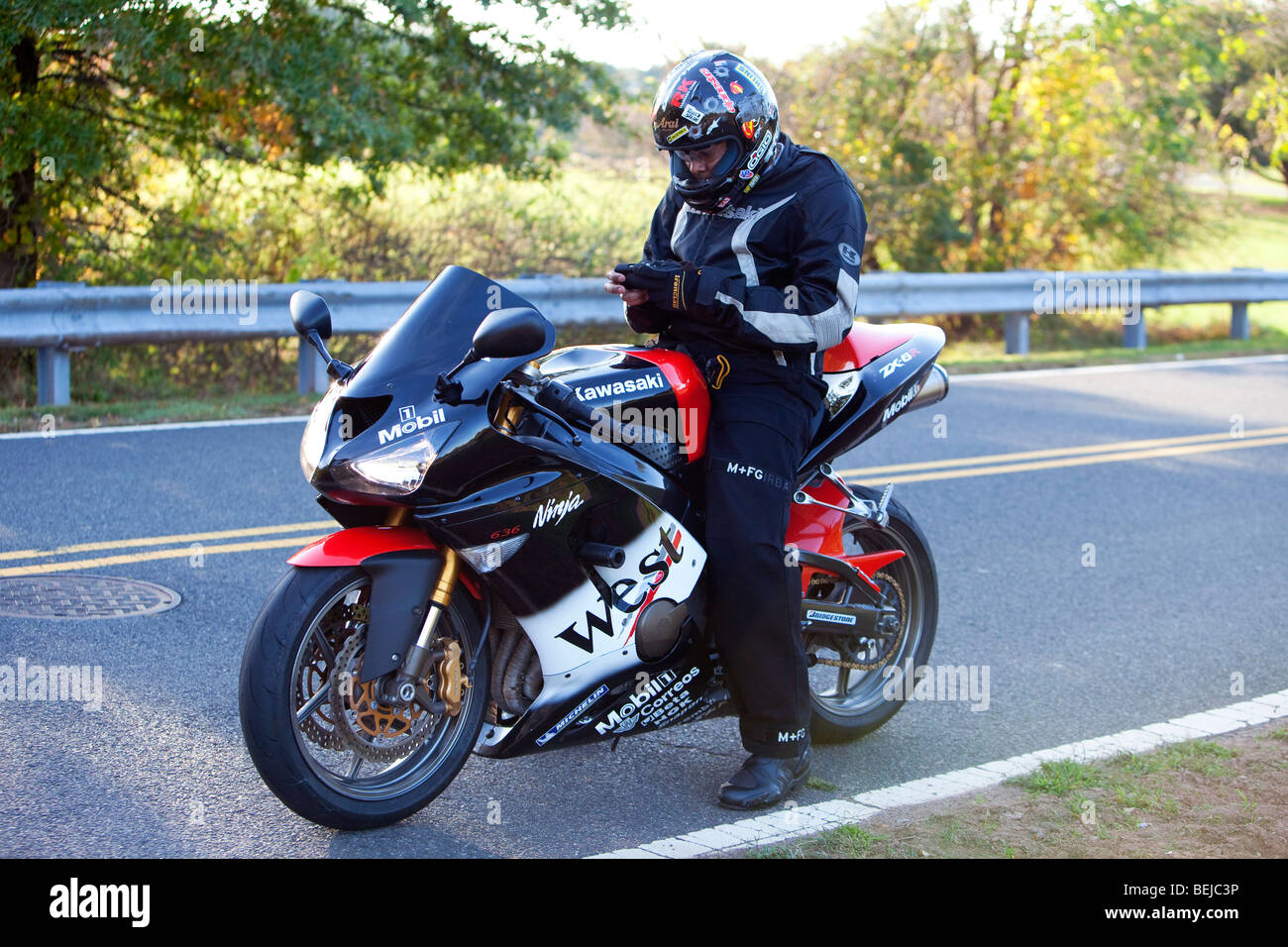 A Kawasaki Ninja with rider pulled of o the side of the road. The ride with  helmet on is checking his messages on Blackberry Stock Photo - Alamy